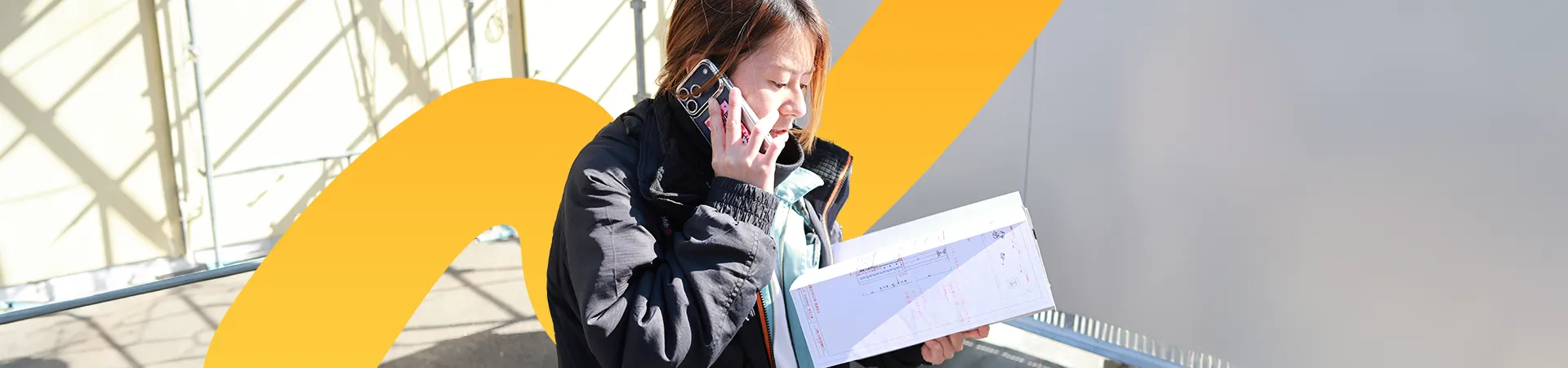 設計図を見ながら電話する女性スタッフ