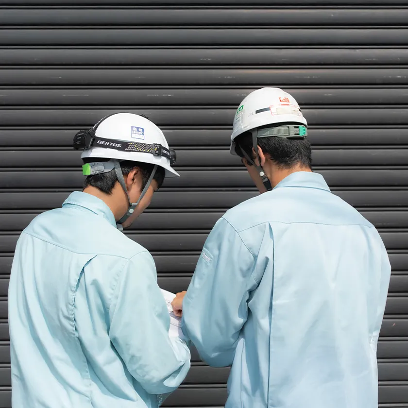 ヘルメット姿のスタッフ2人が電気工事の図面を確認する様子